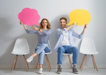 Dva lidé, sedící na židli s papírovými bublinami v rukou.