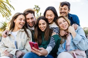 Skupina mladých lidí kouká na telefon.